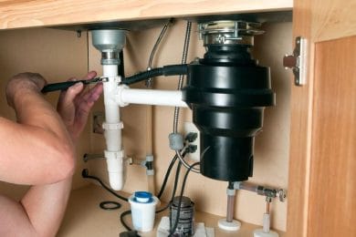 Plumber repairing a garbage disposal beneath a kitchen sink in Sun City Center